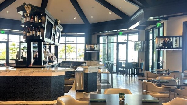 Un'ampia area interna con soffitto alto, una zona bar centrale con televisore e diverse disposizioni di posti a sedere.