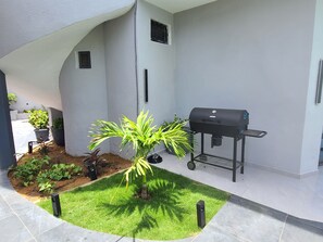 A patio area with a small lawn, a grill, and potted plants.