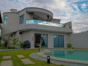 A modern two-story house with a swimming pool, large windows, and a covered outdoor area.