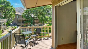A balcony with a table and chairs, overlooking a landscaped area with trees and buildings. - Cozy 2BR Ogden Condo - Pool, Trails, Snowbasin (Ogden)