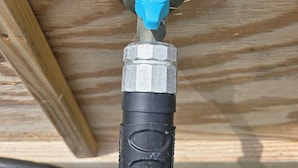 A close-up of a black water spigot with a blue handle, attached to a wooden structure.