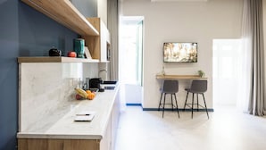 A modern kitchen with marble countertops, a built-in oven, and a dining area with two chairs and a TV. - Buena Vista Suites (Sliema)