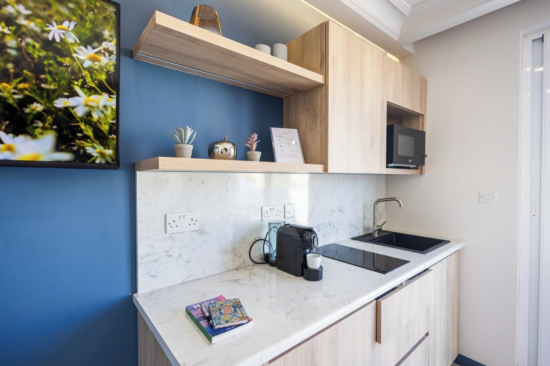 A compact kitchen with a marble countertop, a coffee maker, a microwave, and a sink.