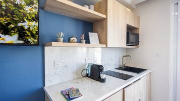 A compact kitchen with a marble countertop, a coffee maker, a microwave, and a sink.