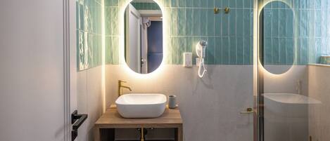A bathroom with a wooden vanity, a white sink, a mirror, and a shower area.