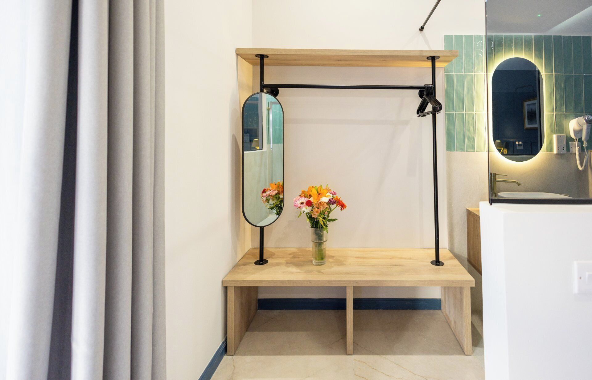Un baño con un banco de madera, un espejo y un florero con flores.