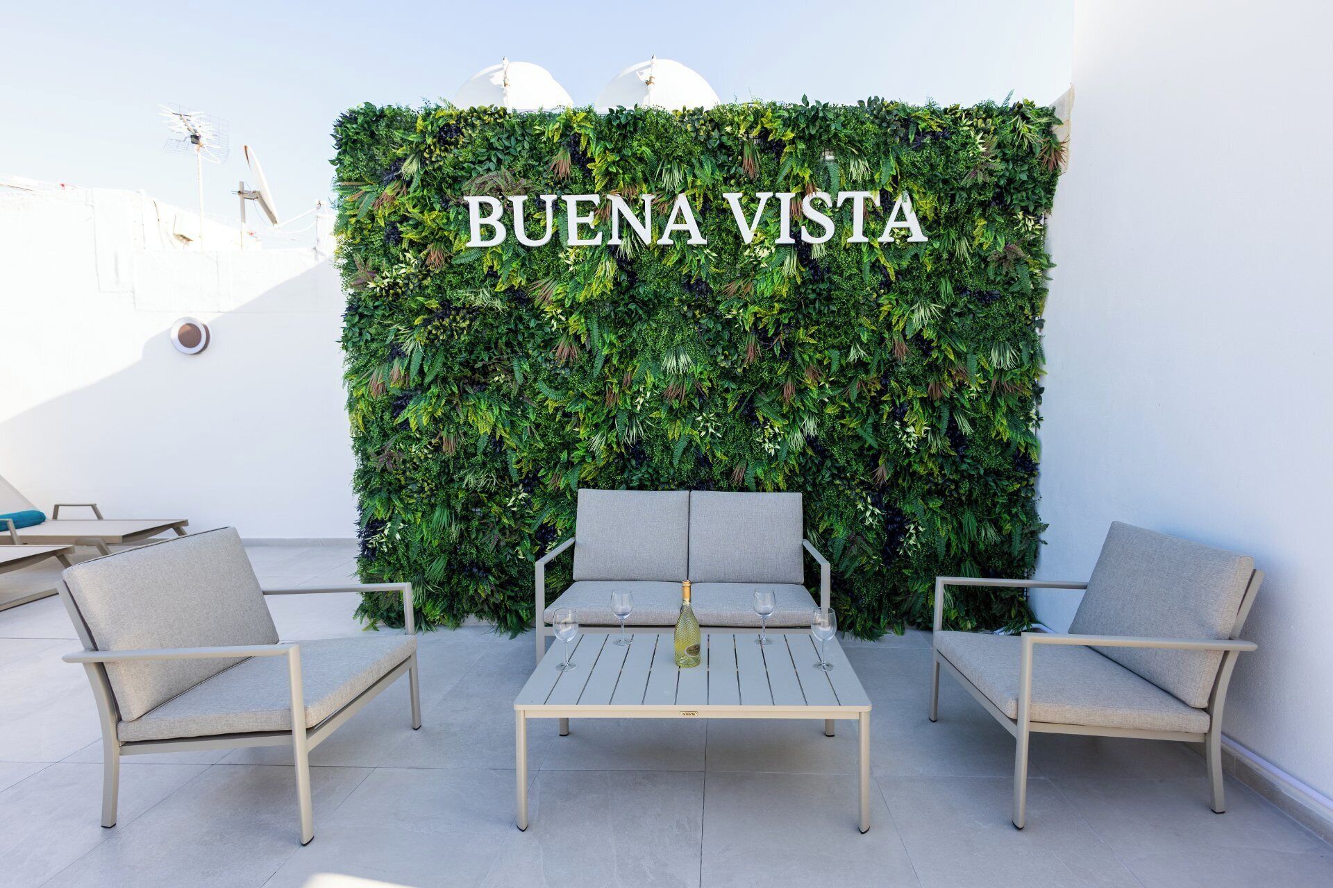Un espace patio agrémenté d’un mur végétal vertical, d’une table avec deux chaises et d’une enseigne indiquant « BUENA VISTA ».
