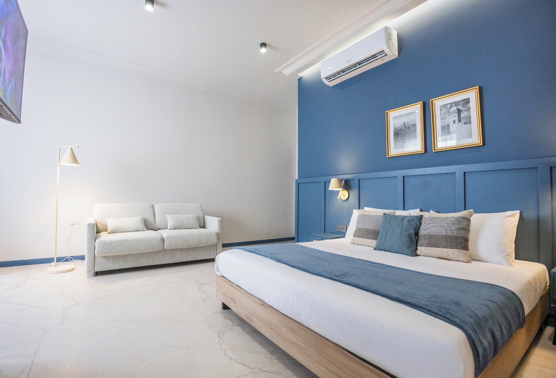 A bedroom with a bed, a sofa, and an air conditioning unit on the wall.