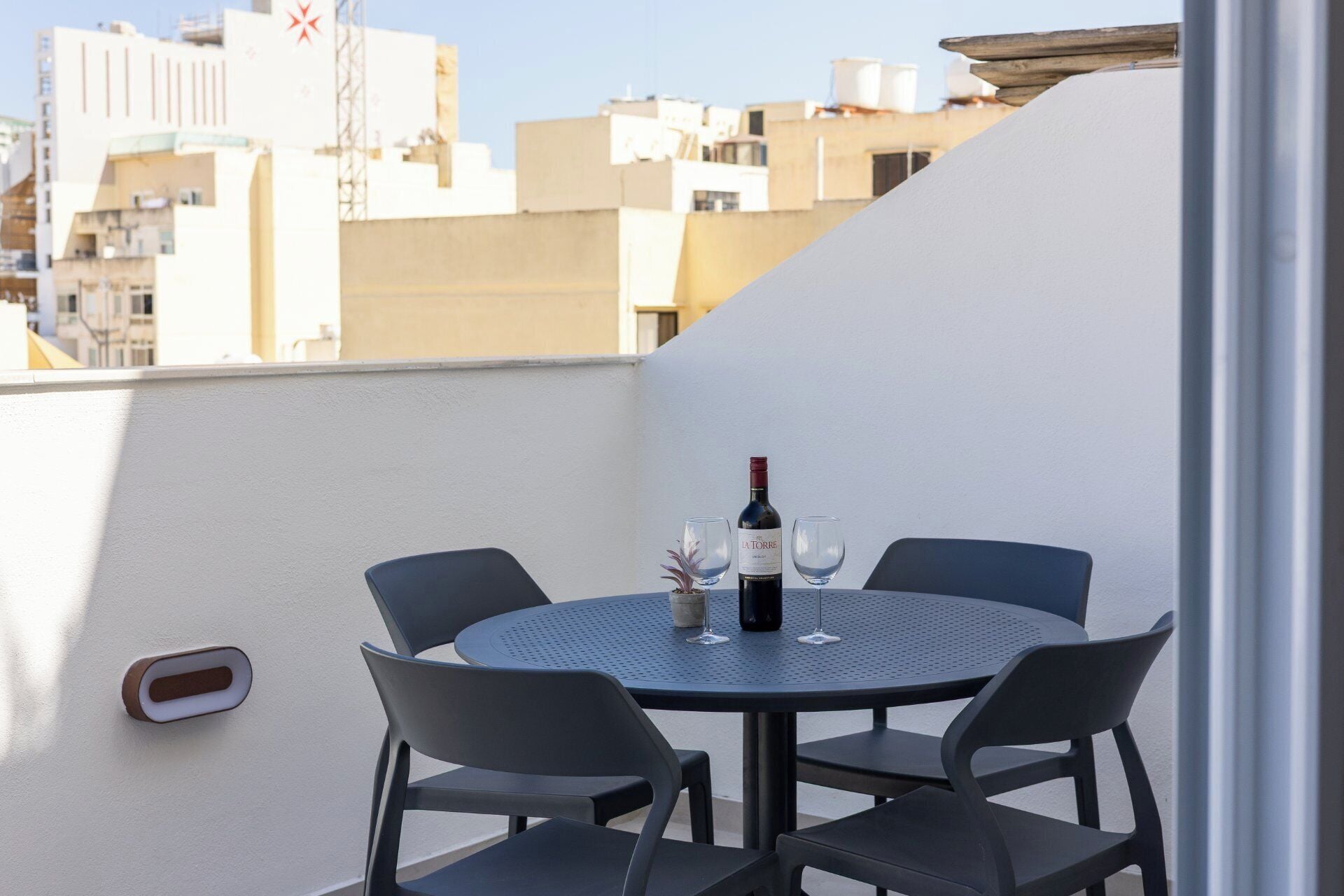 Una mesa redonda con cuatro sillas en un balcón, una botella de vino y dos copas.