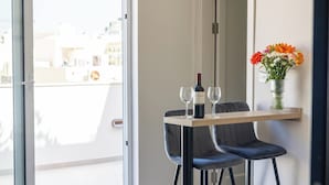A modern room with a balcony, a dining table with two chairs, a bottle of wine, and a vase of flowers. - Buena Vista Suites (Sliema)