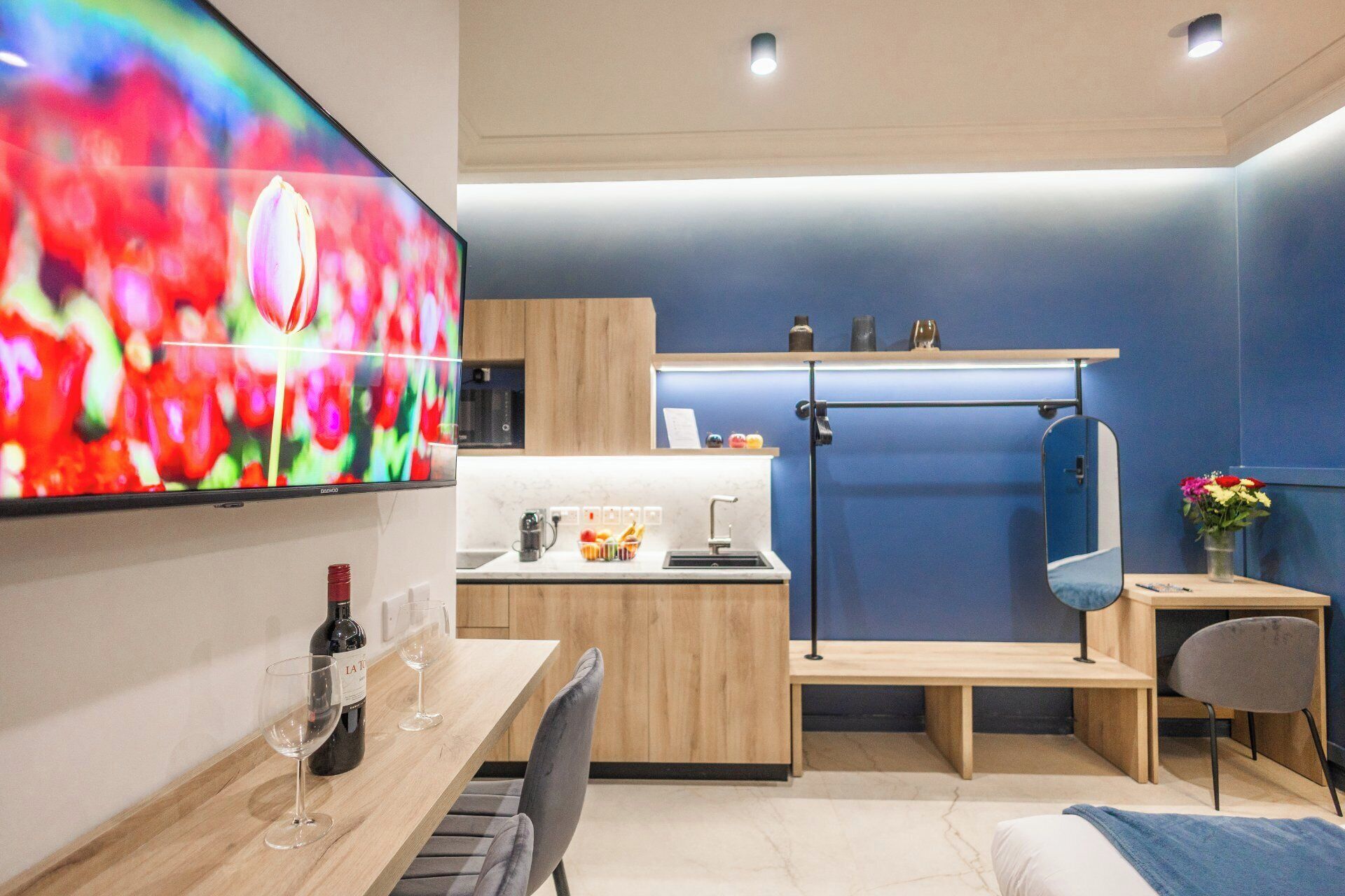 A modern kitchen with a TV, wooden cabinets, a sink, and a dining area with a table and chairs.