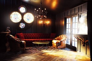 A cozy room with a red sofa, a glass coffee table, and a vintage armchair. There are three stained glass windows and a chandelier. - Cozy 1-bedroom bungalow in welcoming Topanga with AC and fitness room (Topanga)
