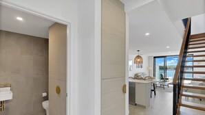 A modern interior with a bathroom, kitchen, dining area, and a staircase leading to an upper level.