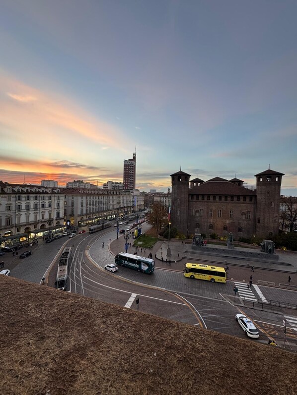 A cityscape with a prominent building featuring two towers, a tram line, and a bus station. - BELVEDERE PALAZZO MADAMA (Torino)