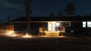 Une maison avec un porche à l’avant, une terrasse en bois et un petit jardin devant.
