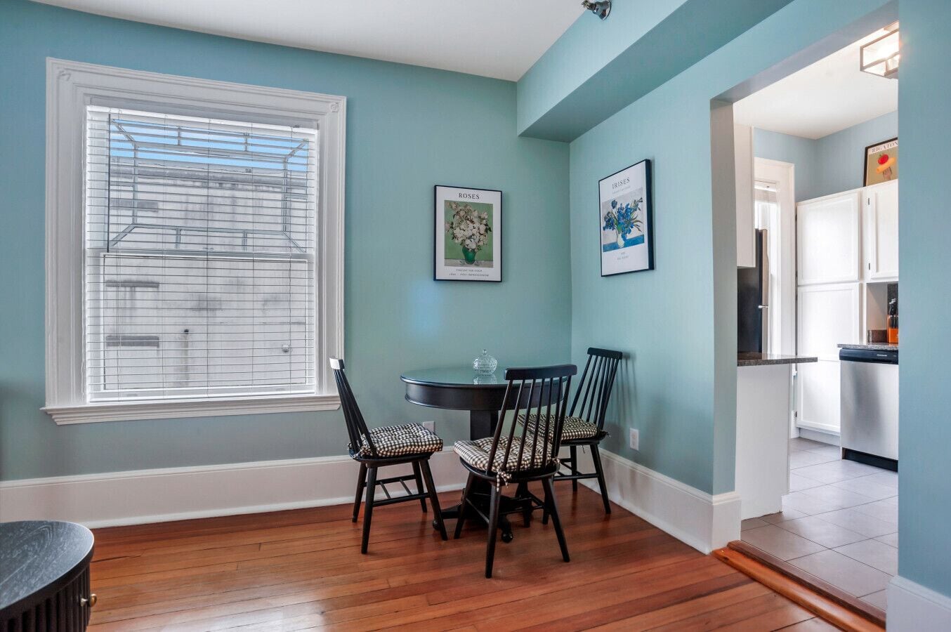 A dining area with a round table, four chairs, and two framed botanical prints on the wall.