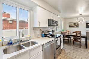 Een moderne keuken met roestvrijstalen apparatuur, witte kastjes en een eethoek met houten stoelen.