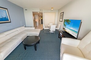 A modern living room with a sofa, a coffee table, a TV, and a dining area with chairs and a table. - Best Ocean Front Views - Oceans One 12th Floor (Myrtle Beach)