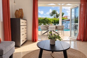 A room with a sofa, a table with a plant, a cabinet, and a view of a pool and outdoor seating area. - Quietly located vacation villa with a private pool (Fontein)