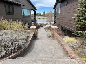 A pathway leading to a building with a view of a lake, surrounded by shrubs and a small tree. - Beautiful end unit home with big horizon views! (Bend)