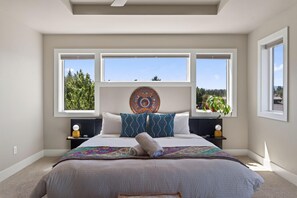A bedroom with a large bed, two bedside tables, a ceiling fan, and three windows with a view of trees and a clear sky. - Beautiful end unit home with big horizon views! (Bend)