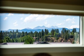 A mountain landscape through a window with a view of a forested area and a building. - Beautiful end unit home with big horizon views! (Bend)