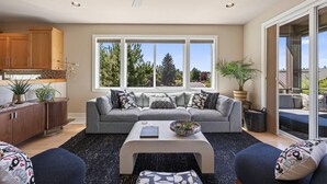 A modern living room with a grey sofa, a coffee table, and a view of trees through large windows. - Beautiful end unit home with big horizon views! (Bend)