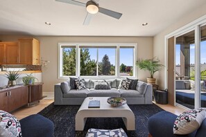 A modern living room with a grey sofa, a coffee table, and a view of trees through large windows. - Beautiful end unit home with big horizon views! (Bend)