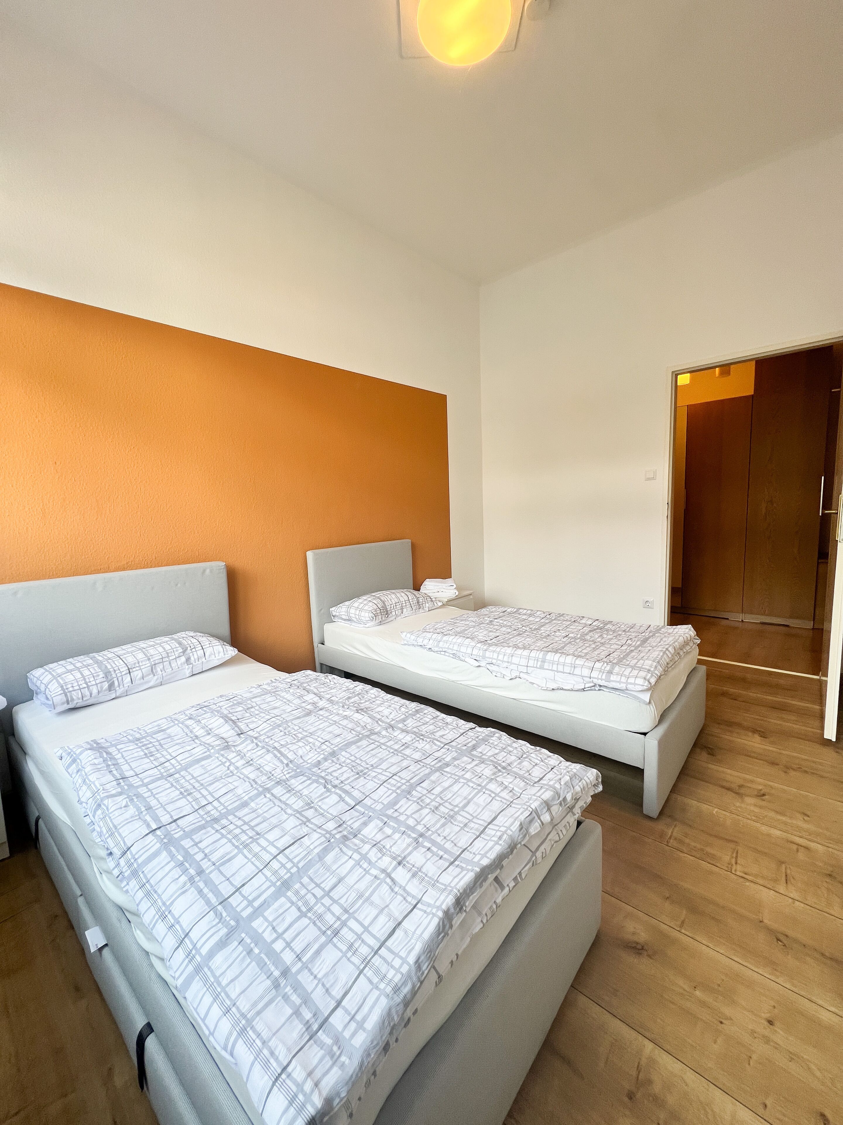 Una habitación con dos camas, piso de madera y una puerta que da a otra habitación.