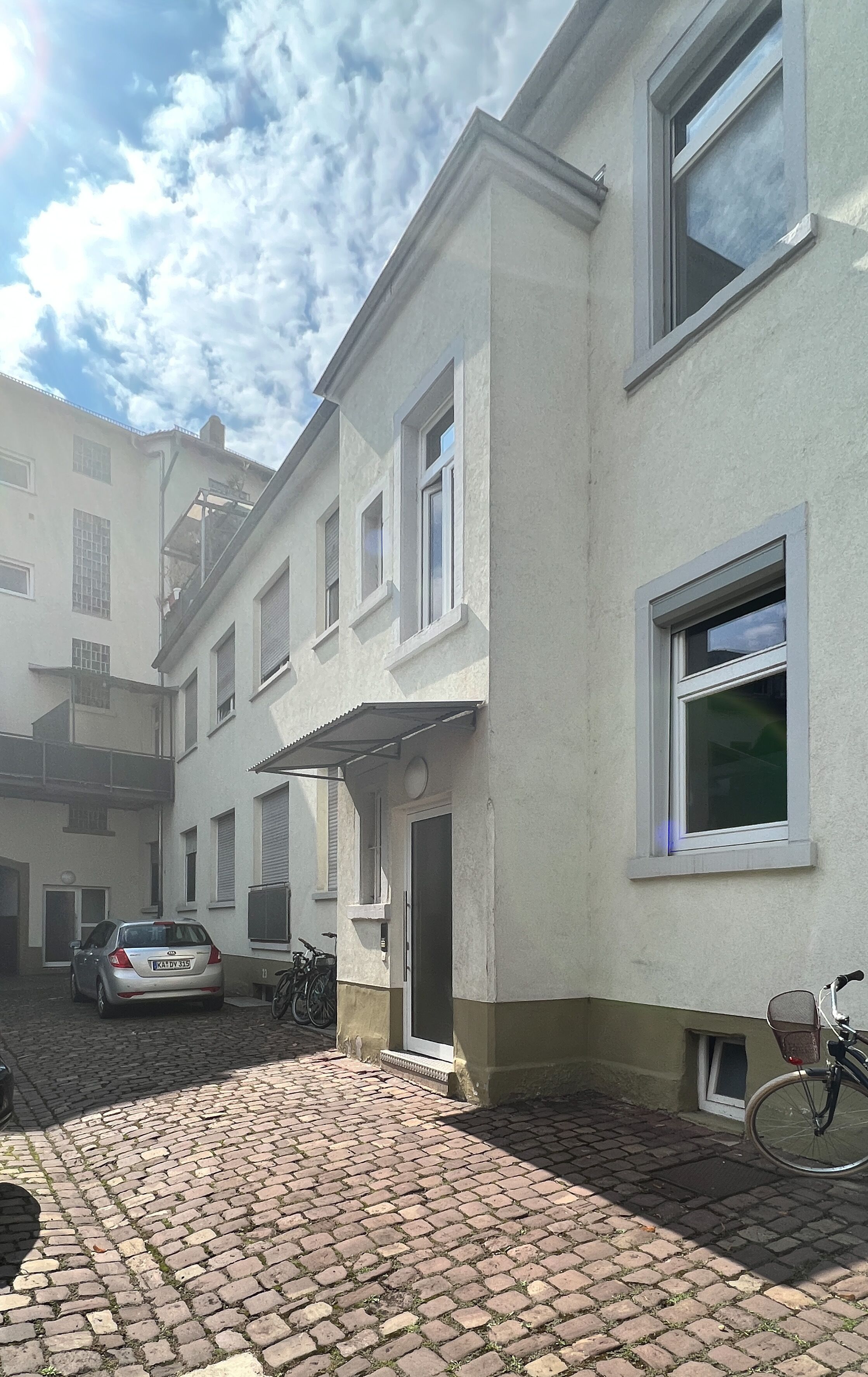Een gebouw met een terras van bakstenen, een auto ervoor en een fiets tegen de muur geleund.