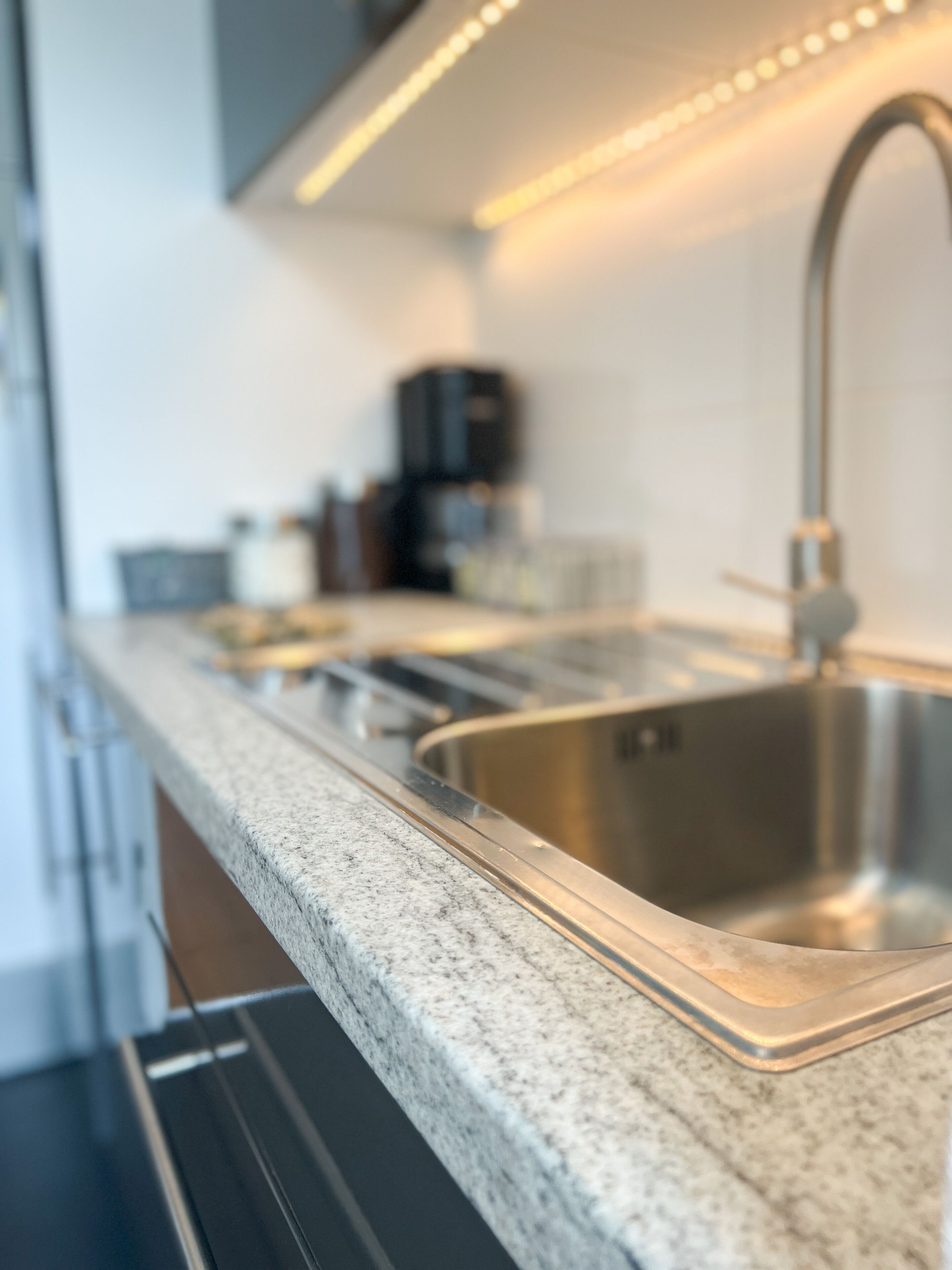 Eine moderne Küche mit einer Granit Arbeitsplatte, einer Edelstahl-Spüle und Deckenleuchten.