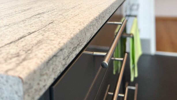 Una cocina moderna con encimera de granito, electrodomésticos de acero inoxidable y una toalla verde colgada en un tendedero.