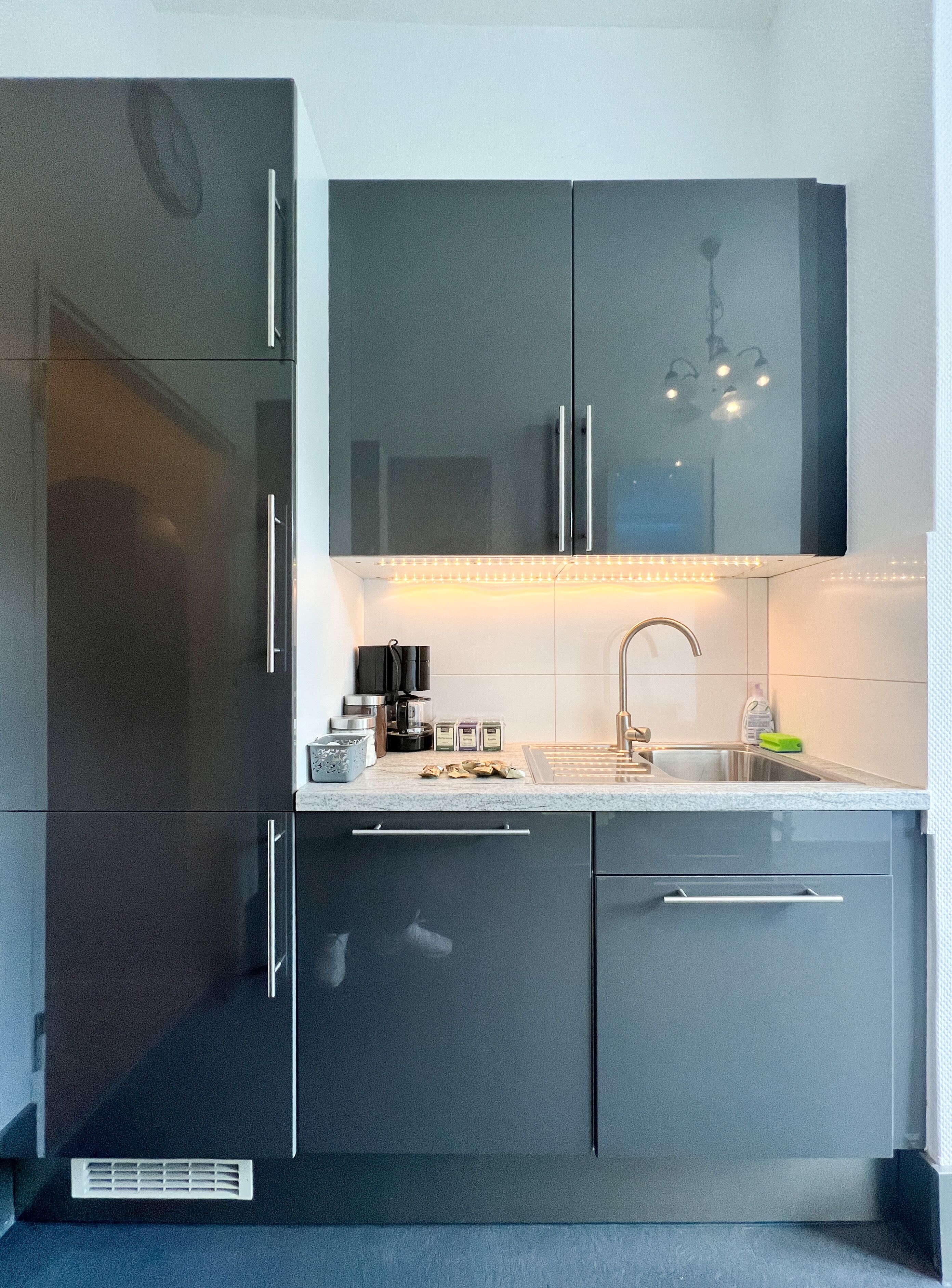 A modern kitchen with dark cabinets, a stainless steel sink, and a built-in coffee machine.