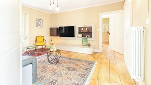 Ein Wohnzimmer mit Fernseher, einem gelben Sessel, einem gemusterten Teppich und einem weißen Schrank.