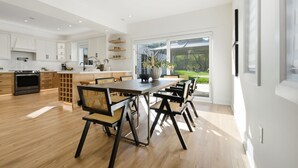 A modern kitchen with wooden cabinets, a central island, and a dining area with black chairs and a wooden table. - Lake Simcoe Ice Fishing Basecamp • Sleeps 10–12 • Heated Shop (Beaverton)