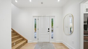 A clean, modern entryway with a wooden staircase, a white door, and a rug on a wooden floor. - Lake Simcoe Ice Fishing Basecamp • Sleeps 10–12 • Heated Shop (Beaverton)