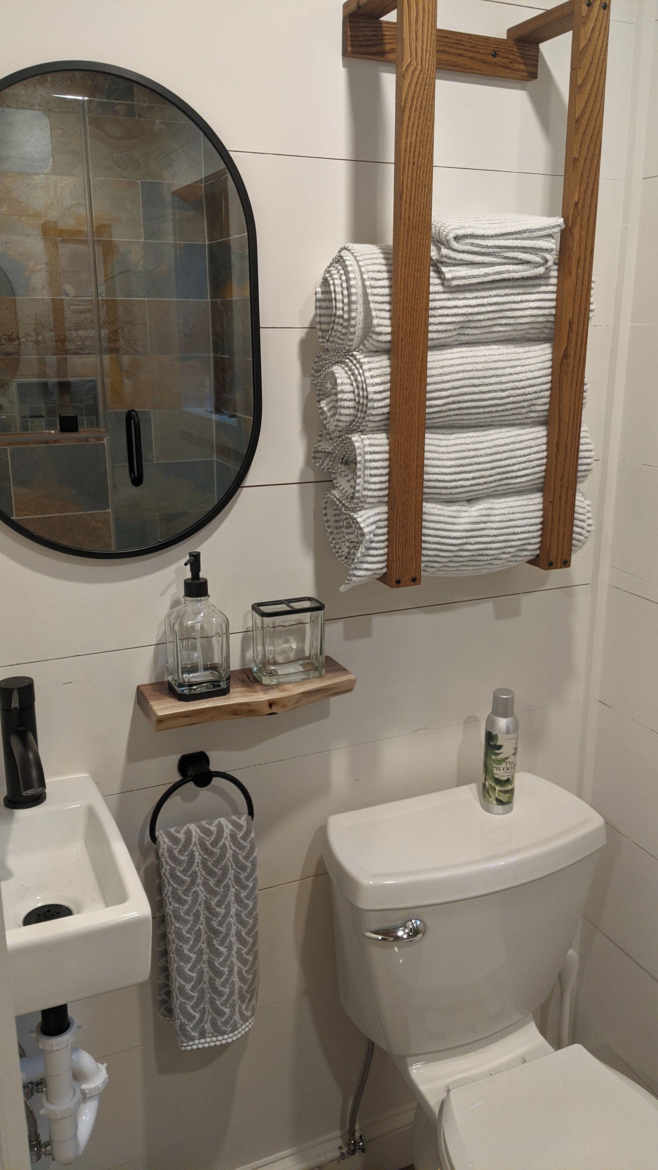 A bathroom with a toilet, sink, and mirror. There are towels and a soap dispenser on the wall.