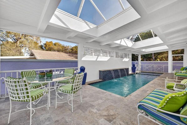 Uma área de piscina interna com mesa e cadeiras de vidro, uma piscina e vista para o exterior.