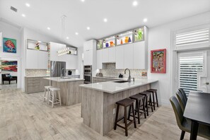 Een moderne keuken met witte kasten, een groot eiland met krukken, en een eetgedeelte met een tafel en stoelen.