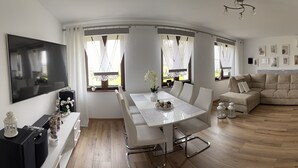 Ein modernes Wohnzimmer mit Esstisch in Weiß, einer Couch und einem an der Wand befestigten Fernseher.