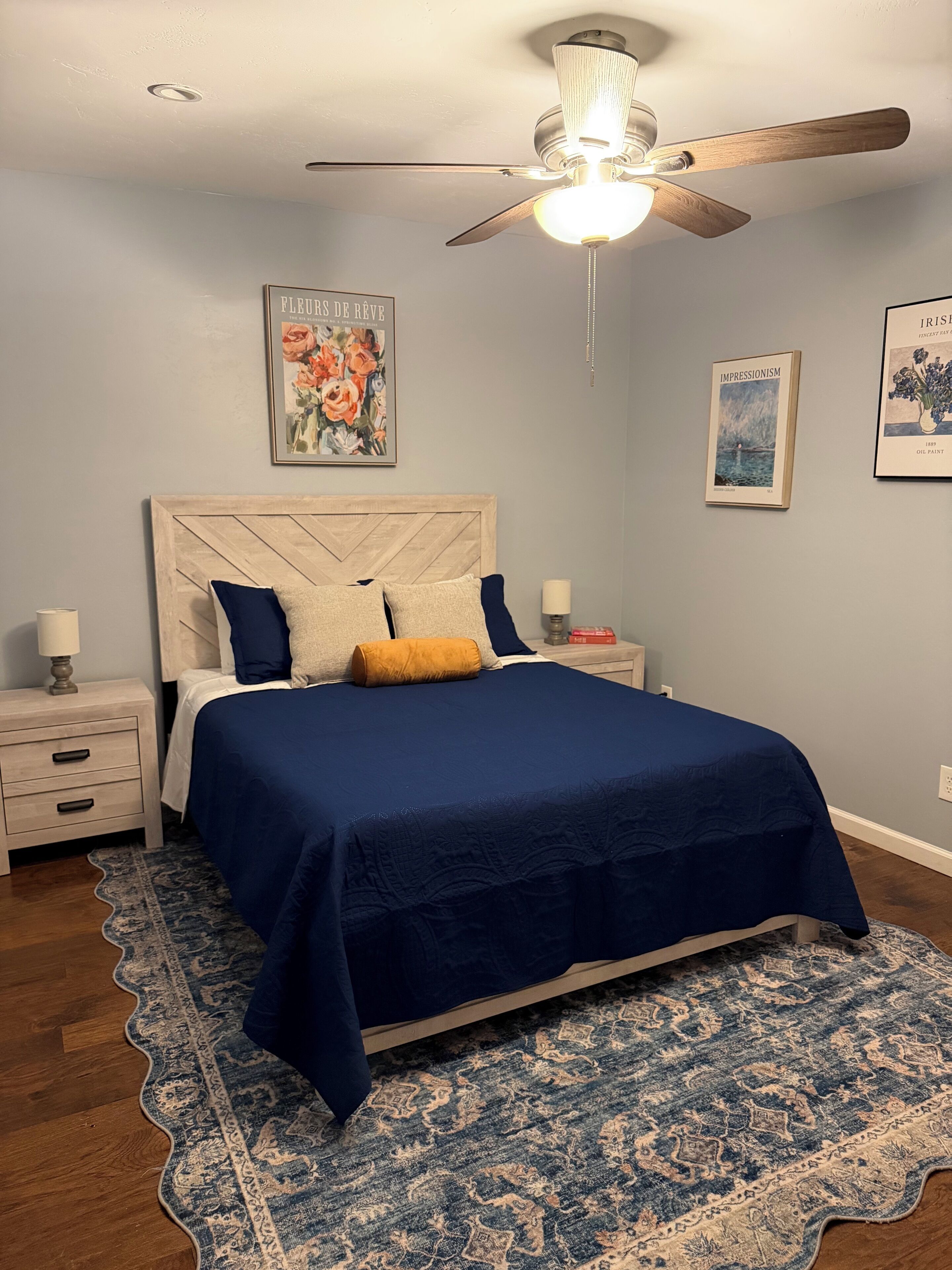 Une chambre à coucher comprenant un lit, des tables de chevet, un ventilateur de plafond et des œuvres d’art murales.