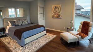 Ein Schlafzimmer mit einem Bett, einem Sessel, einem Deckenventilator, einem großen Fenster und einem Buddha-Gemälde.