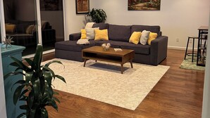 Ein Wohnzimmer mit einem dunkelgrauen Sofa, einem Holztisch und einem großen Fenster.