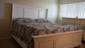 Ein Schlafzimmer mit Bett, Kommode und einem Fenster mit Jalousien.