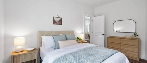 A bedroom with a bed, nightstands, a dresser, a ceiling fan, a door, and a wall-mounted mirror.