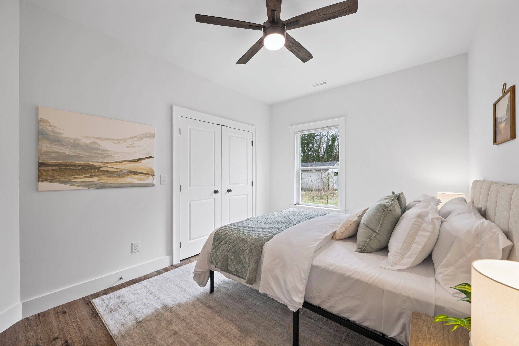 A bedroom with a bed, a ceiling fan, a window, and a door.