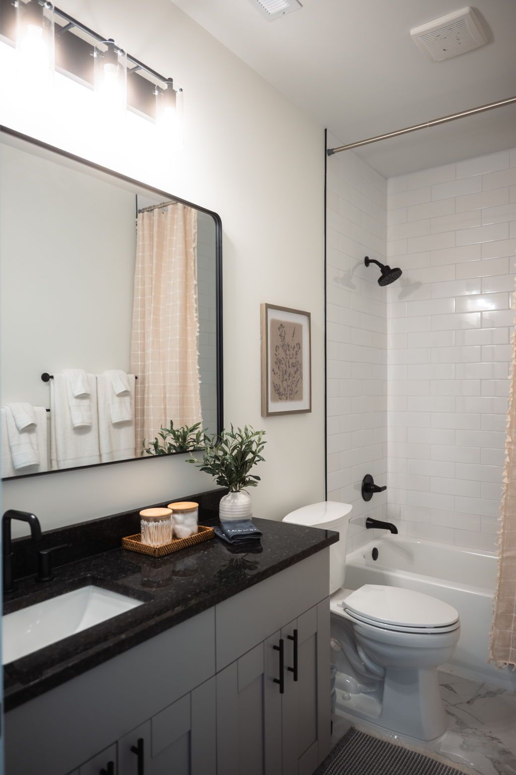 Een moderne badkamer met een zwart aanrecht, een witte wastafel en een toilet. Er is een douche met een glazen deur en een afbeelding in een lijst aan de muur.