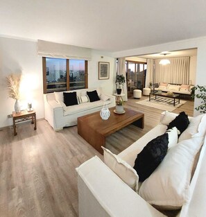 A modern living room with a sofa, coffee table, and a view of the city through large windows. - A beautiful view of Santiago. Apartment for 10 people, just a few steps from Parque Arauco (Las Condes)