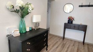 Una stanza con un comò in legno scuro, un tavolino con una lampada, uno specchio e un vaso con fiori sulla parete.