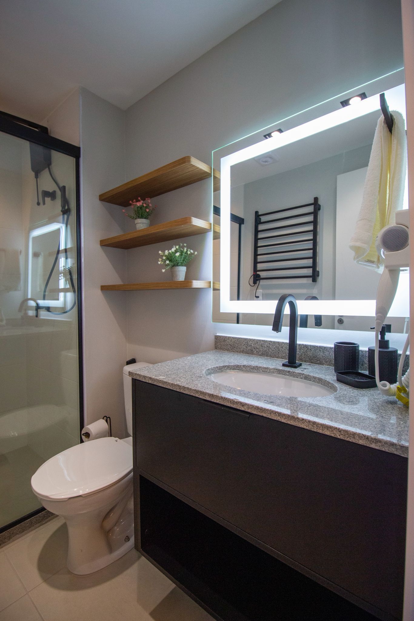 Un baño moderno con cabina de ducha de vidrio, inodoro blanco, tocador con un espejo grande y un secador de pelo en la encimera.